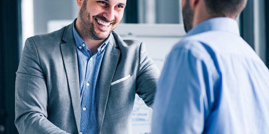 Two smiling businessmen shaking hands while standing in an offic